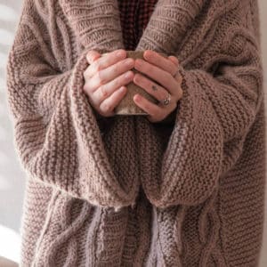 A person wearing cosy clothes cupping a hot drink in their hands